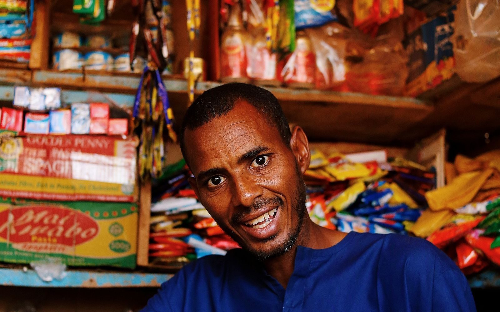 A shop owner standing behind the counter of his neighbourhood kiosk