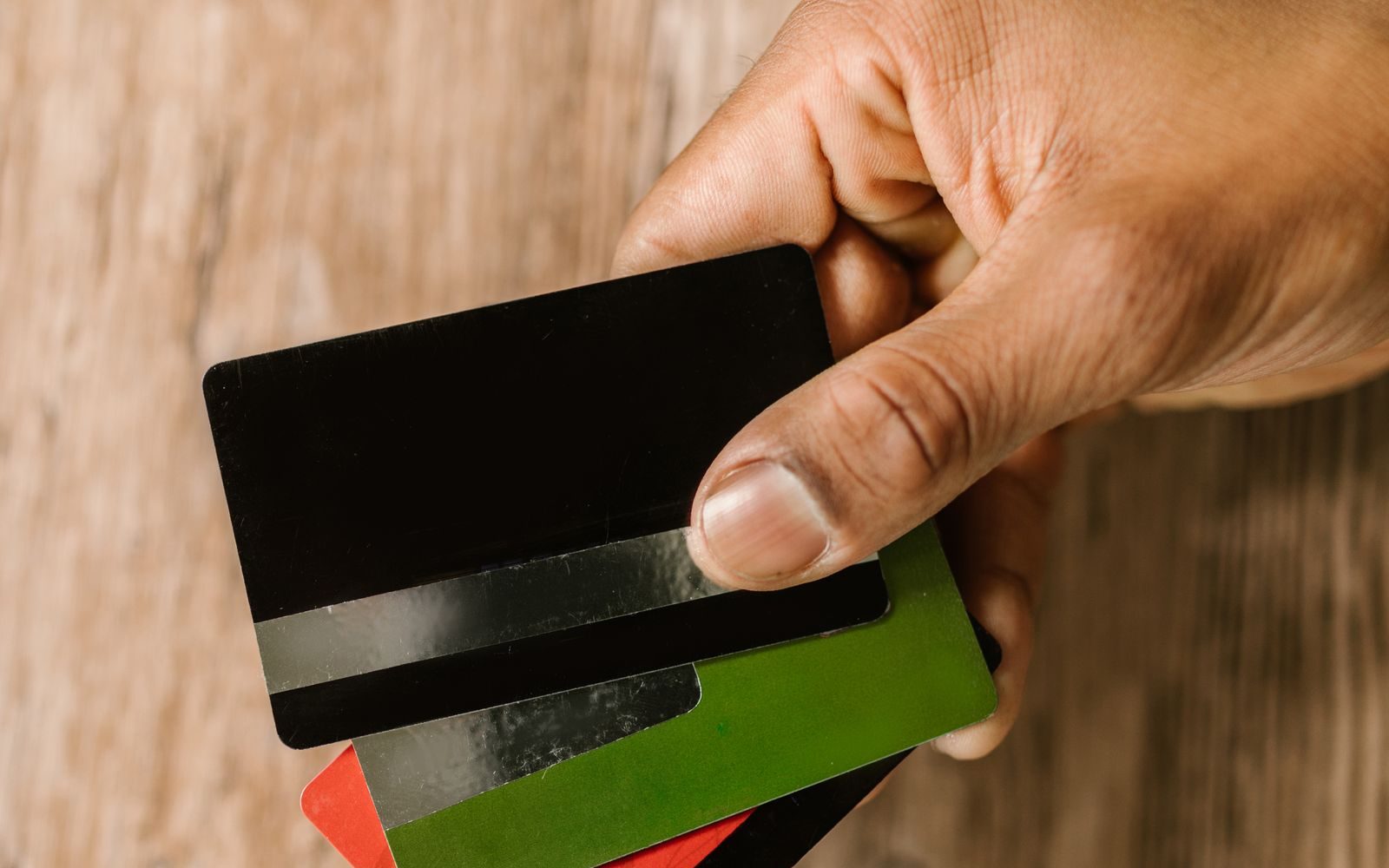 A hand holding a bank card over a wooden table