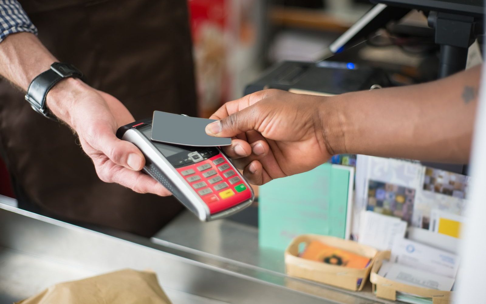 A customer paying by contactless card at a shop counter