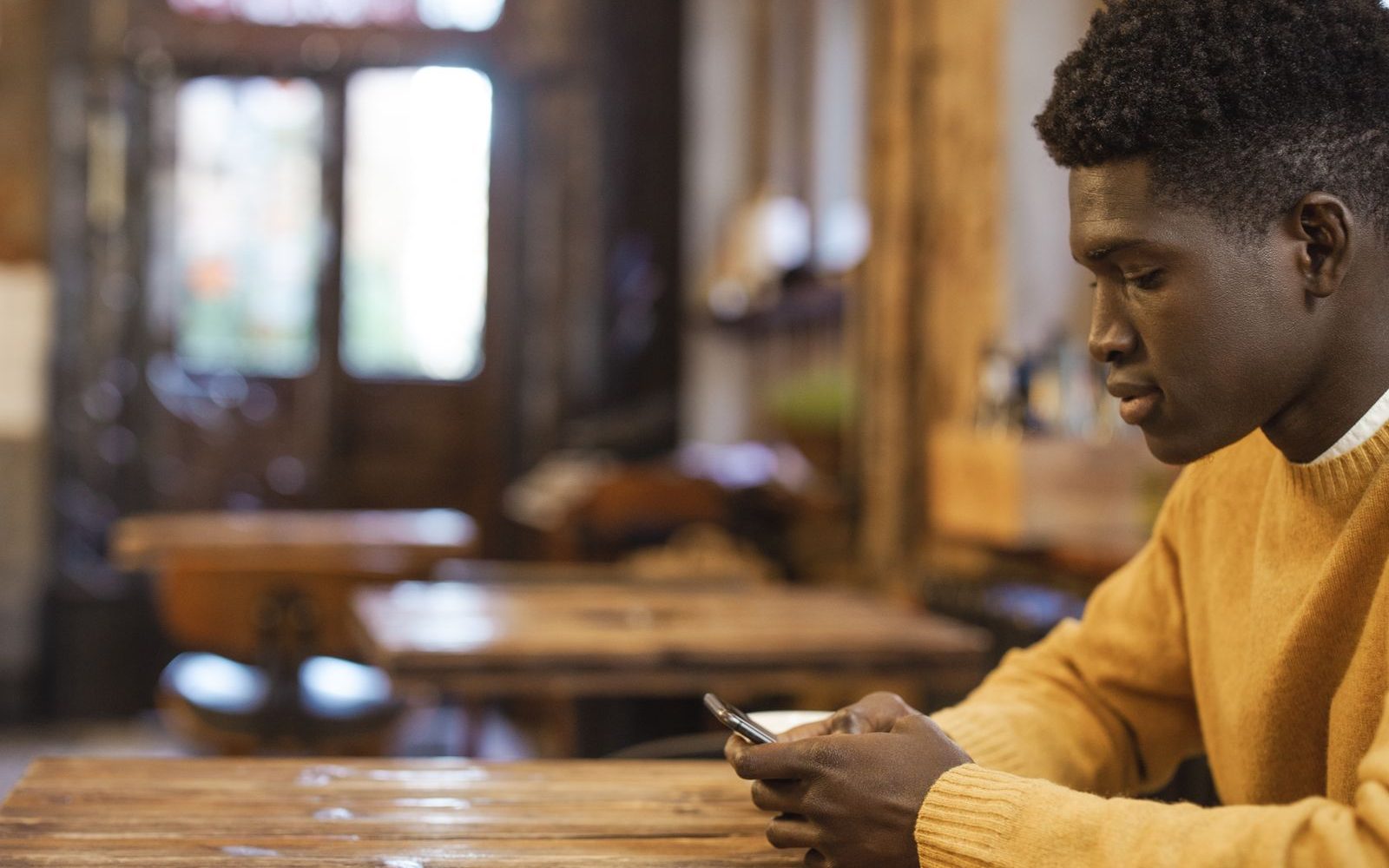 A young Nigerian man checking his bank balance on his phone in a cafe